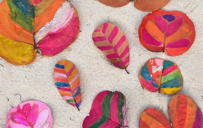 Feuilles d'automne peintes par les enfants, disposées en cercle sur du sable — projet mêlant arts plastiques et découverte des saisons.